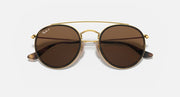 Round sunglasses with gold metal frame and dark brown lenses, double bridge and curved arms.