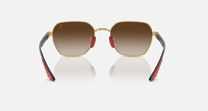 Sunglasses with gold frame and brown lenses, dark arms with red hinge accents.