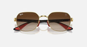 Sunglasses with gold frame and dark brown lenses, red accents near hinge, oval shape.