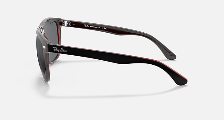 Sunglasses side view with black arms, gray lenses, and red edge trim.