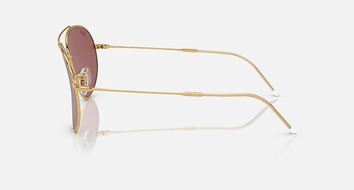 Ray-Ban aviator sunglasses in gold with maroon lenses, side view.