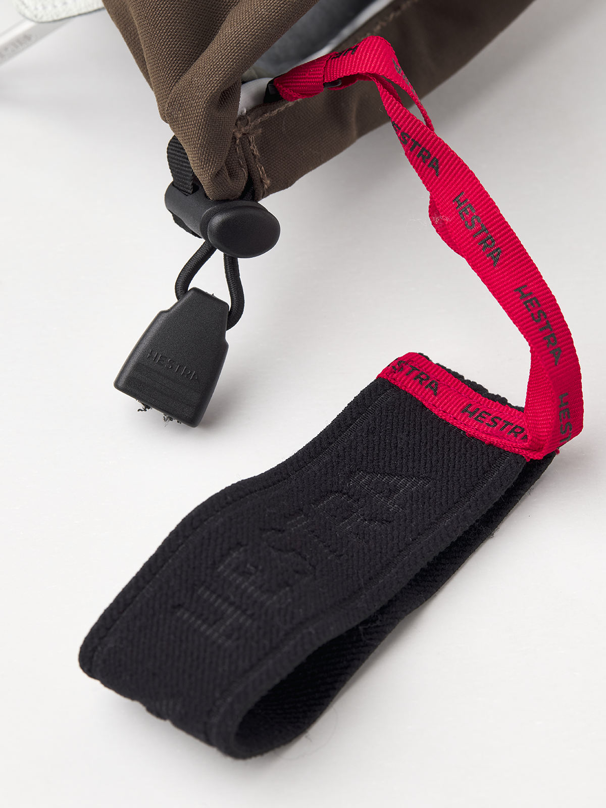 Dark brown Hestra ski mittens with black wrist strap and red logo elastic