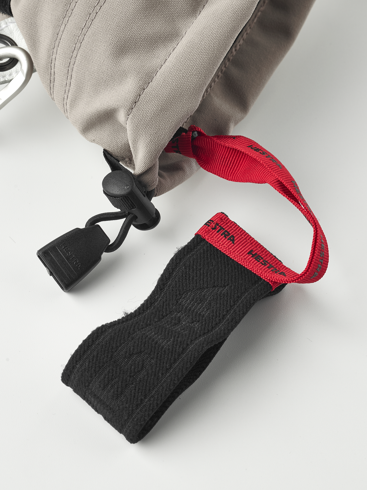 Beige ski mitten with black and red wrist strap and hanging carabiner