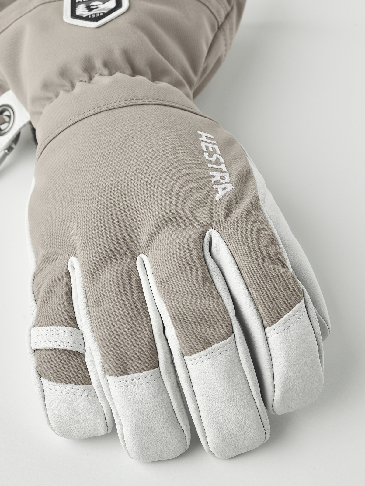Taupe ski glove with white accents and “Hestra” logo on the back.