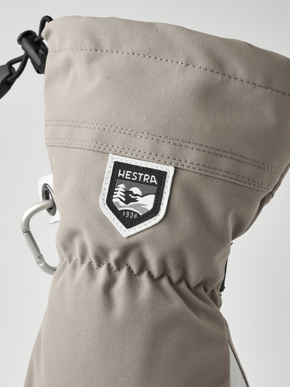 Tan Hestra ski glove with logo patch and metal carabiner-style clip