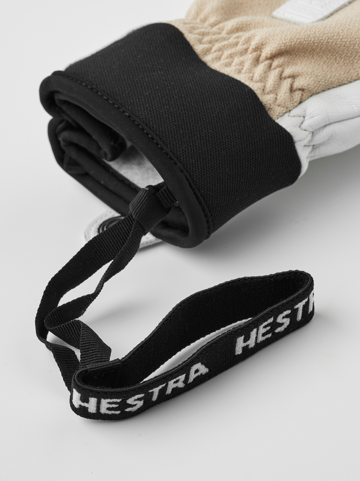 Black glove cuff with woven wrist strap and Hestra lettering, beige glove beneath