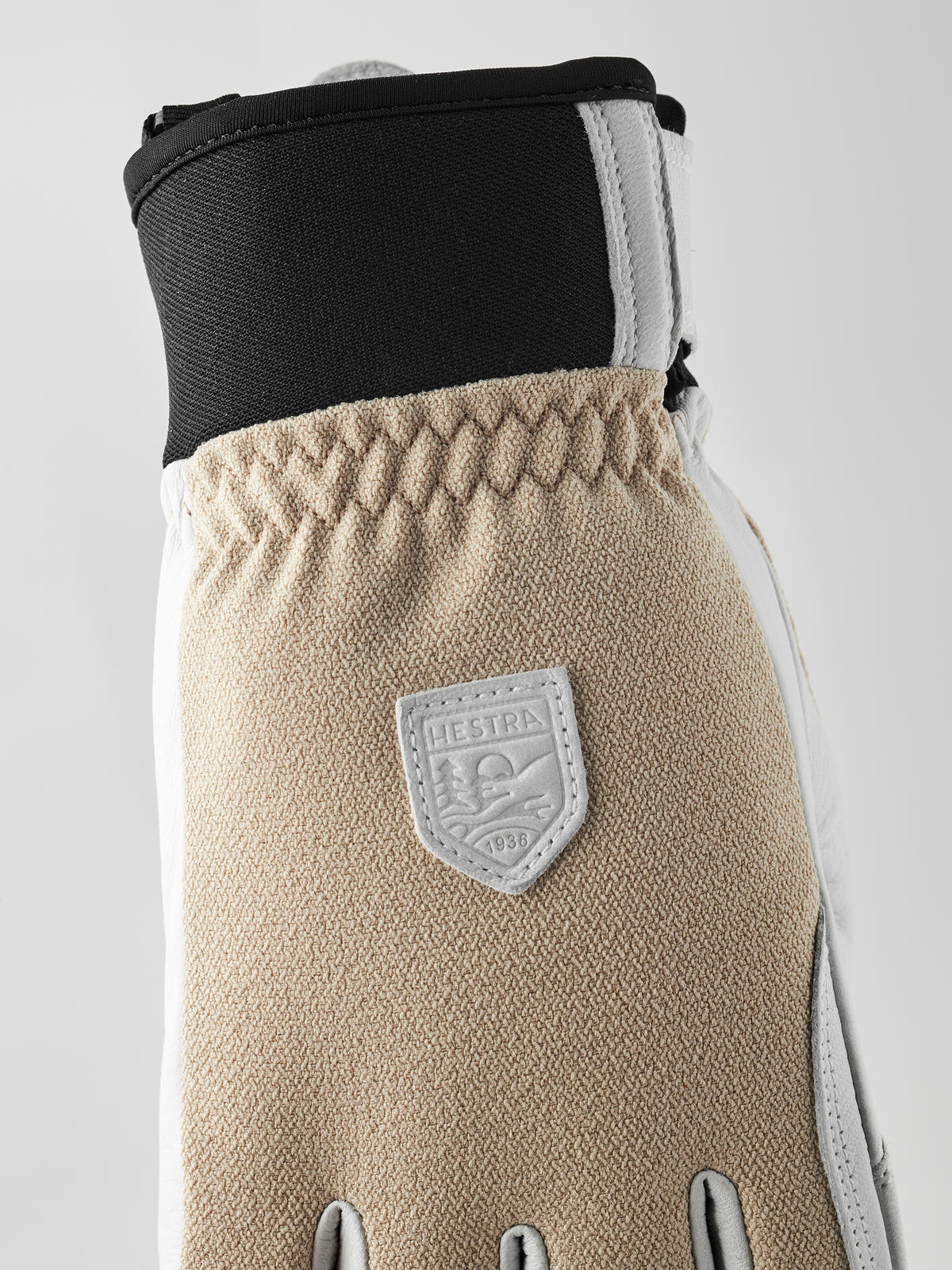 Tan textured patrol glove with dark cuff, Hestra shield patch, and stitched seams