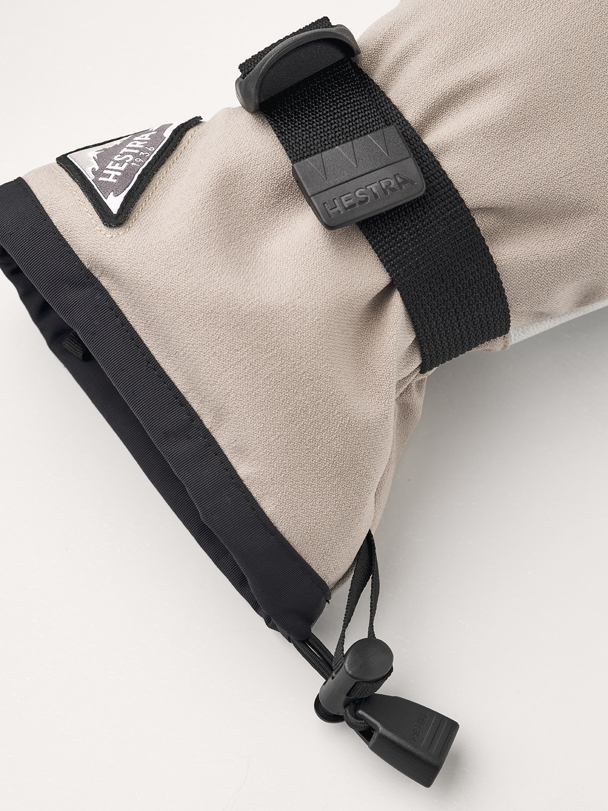 Beige powder gauntlet glove wrist detail with black strap and toggle closure