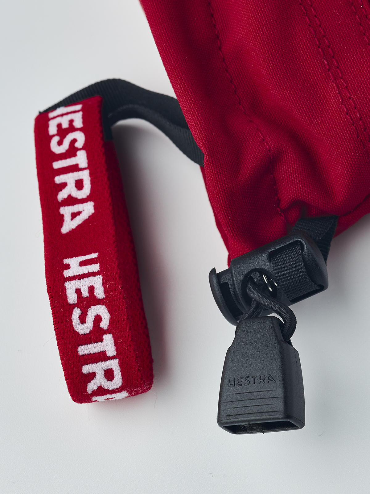 Red ski junior glove cuff loop with HESTRA label and black cord lock
