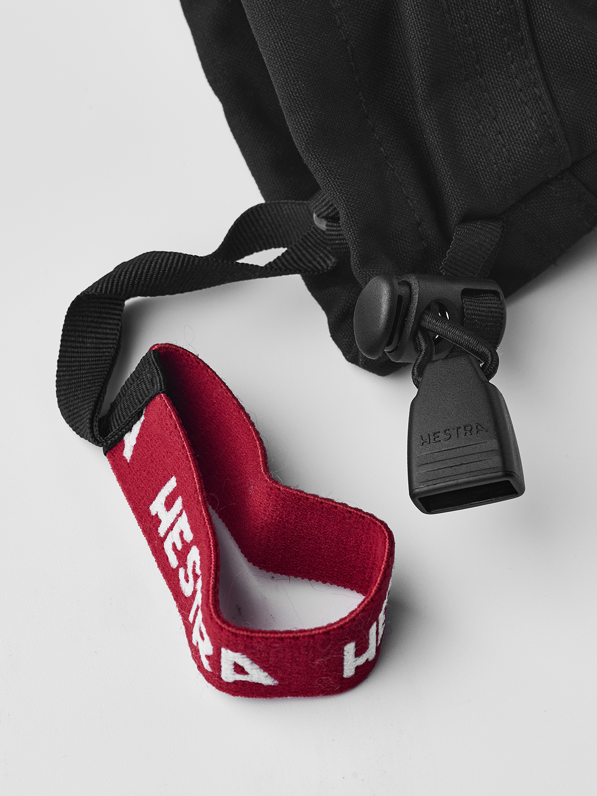 Black junior ski gloves with red wrist strap and hanging Hestra tag