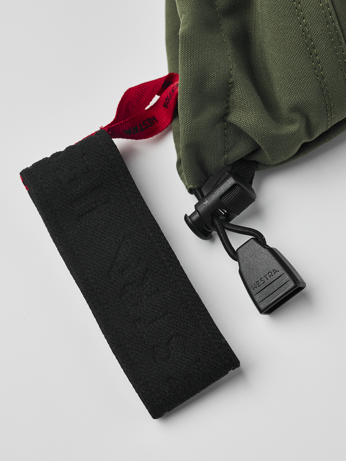 Olive ski glove with black wrist strap and red fabric label inside cuff.