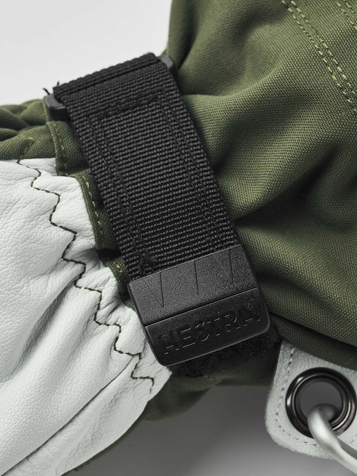 Olive gloves with black wrist strap and pull tab on white leather panel