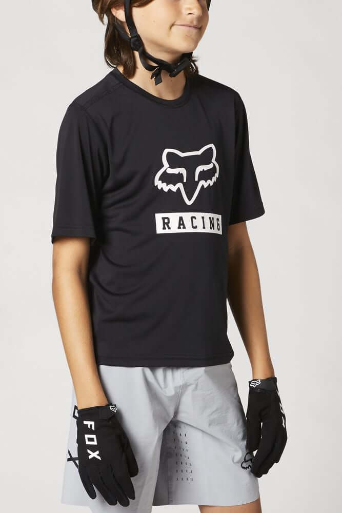 Youth black short-sleeve jersey with white FOX Racing logo; paired with light shorts.