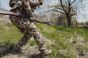 Men's camouflage hunting pants in green-brown pixel print, standing side view.