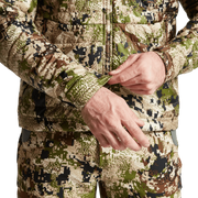 SITKA camouflage hooded jacket detail, hands adjusting zipper pull and pocket edge.