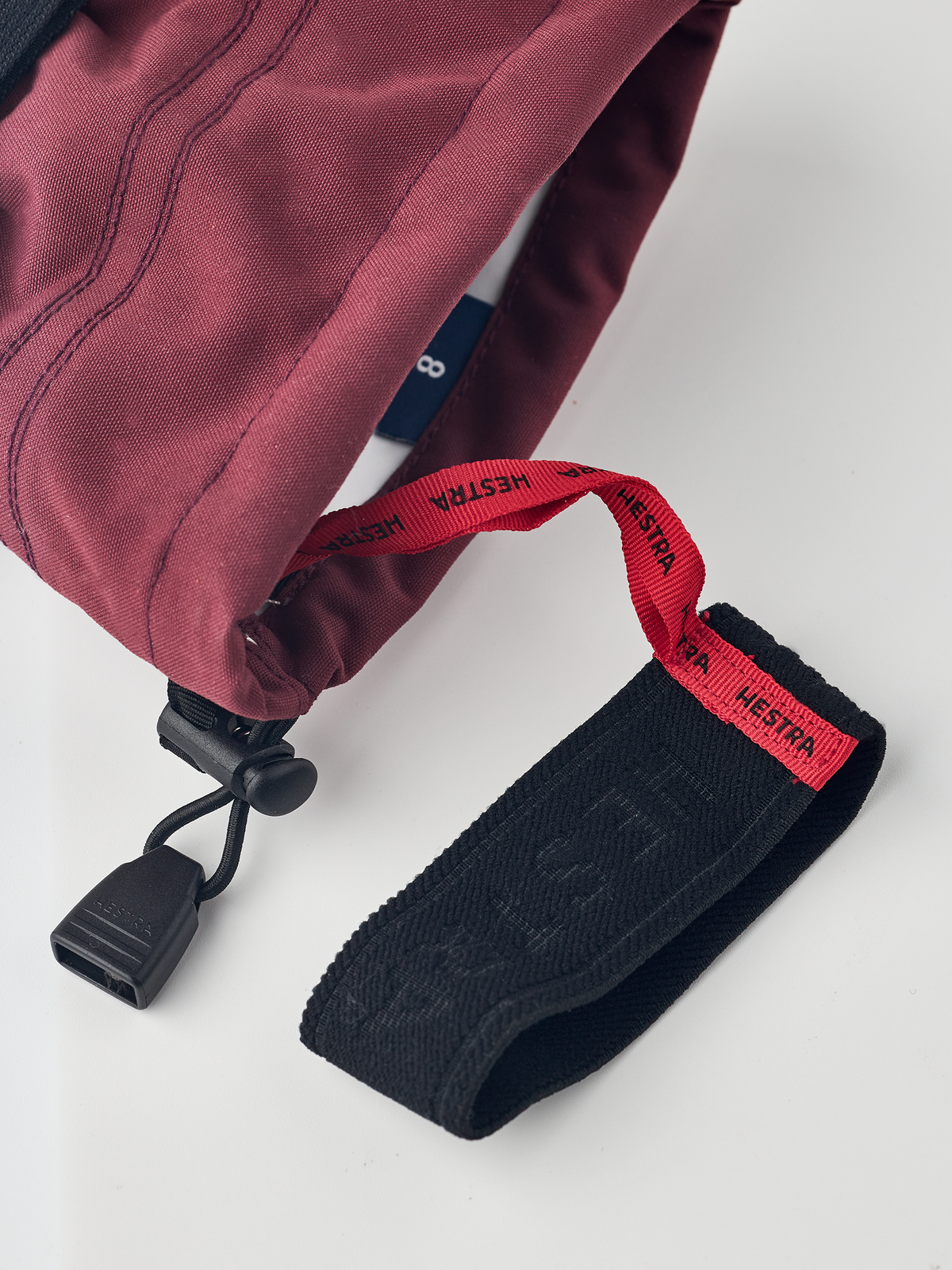 Burgundy ski glove with dark navy textured wrist strap and black drawcord adjuster