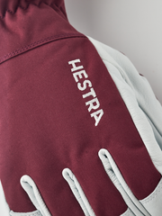 Burgundy ski glove with Hestra logo on textured fabric and white leather trim.
