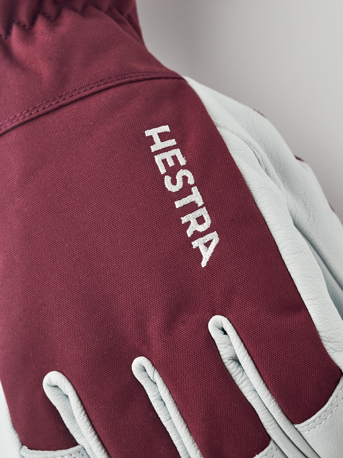Burgundy ski glove with Hestra logo on textured fabric and white leather trim.
