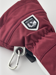 Burgundy ski glove with white logo patch, black drawcord, and metal snap carabiner