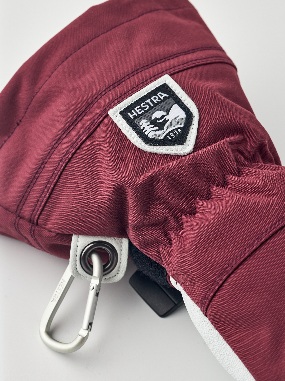 Burgundy ski glove with white logo patch, black drawcord, and metal snap carabiner