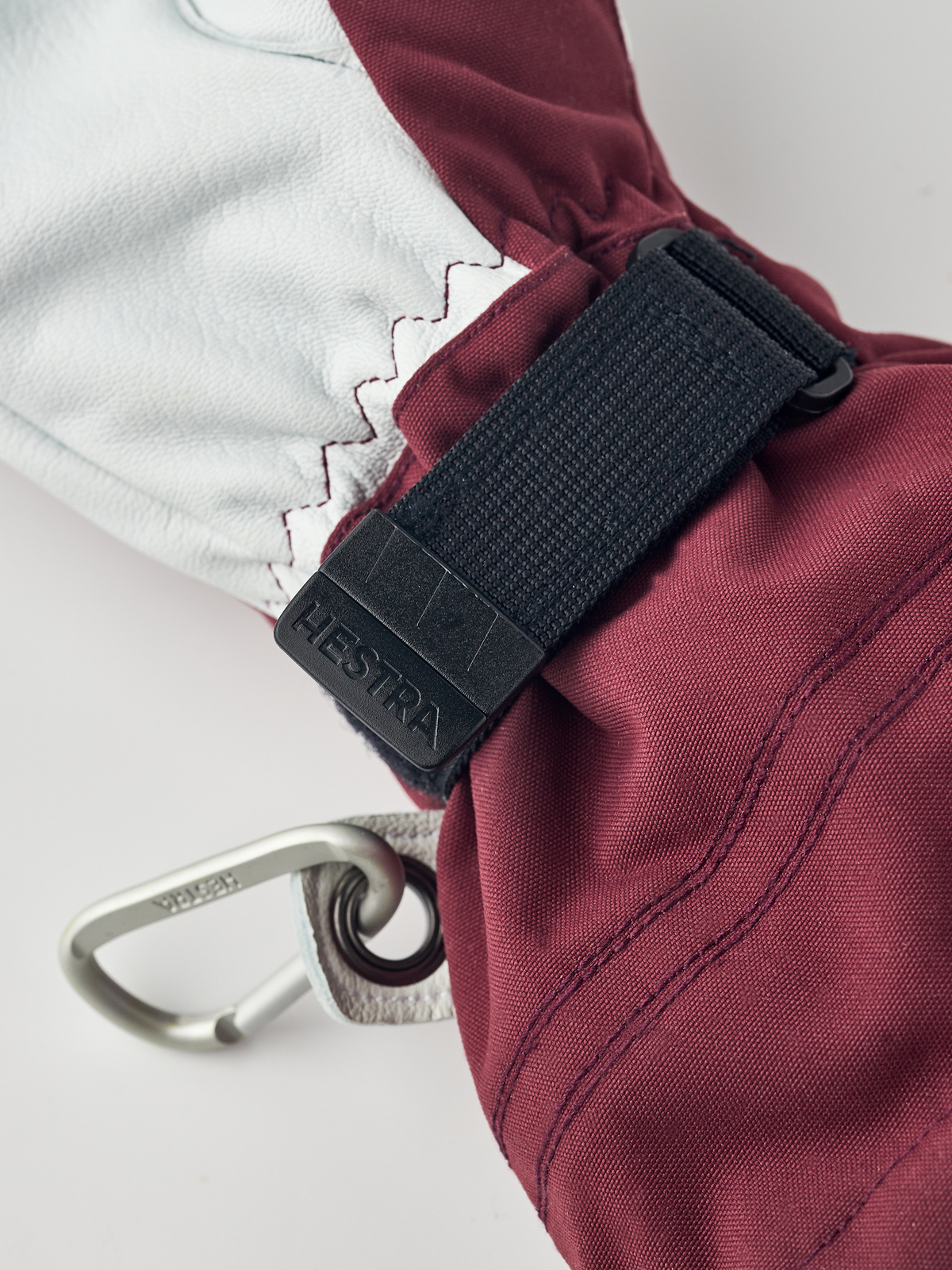 Burgundy ski glove with black wrist strap and metal carabiner clip.