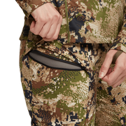 Camo hiking pants detail with zip pocket and hand pulling the zipper tab