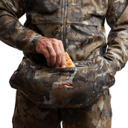 Hand placing inside camo insulated muff; orange pull tab on zipper