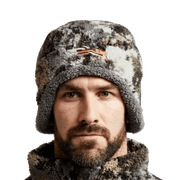 Brown, black, and white camouflage fleece beanie with orange logo on wearer's head