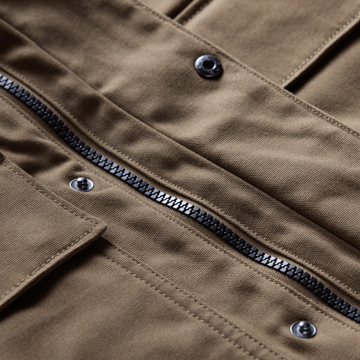 Coyote brown chore coat front zipper close-up with dark metal teeth and buttoned tabs.