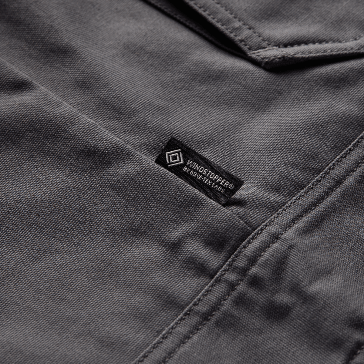 Iron grey chore coat label at chest seam, with stitched collar edge and fabric texture.