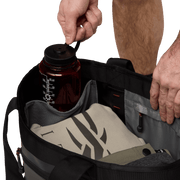 Open black 40L tote bag with bottle, pouch, and hands adjusting the contents