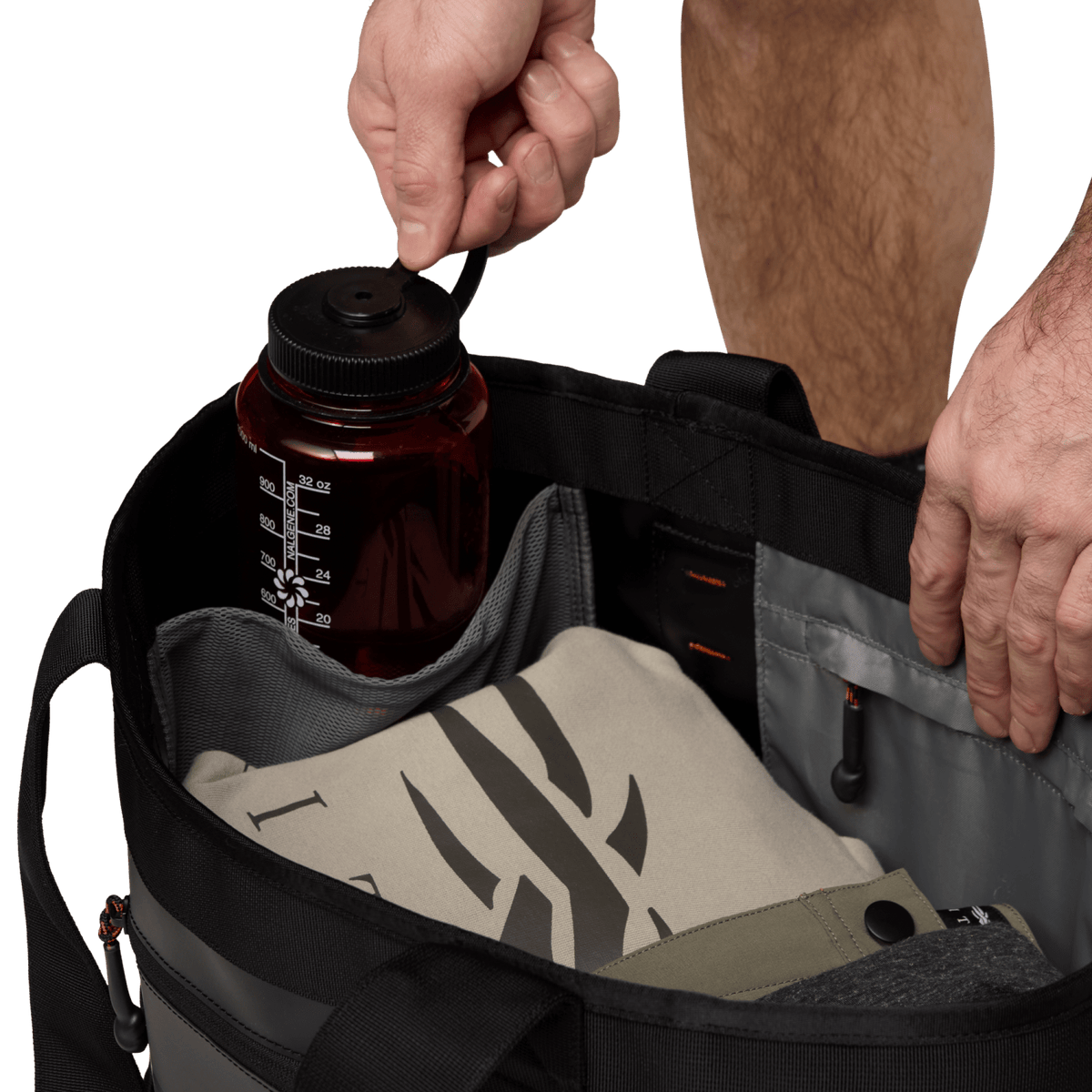Open black 40L tote bag with bottle, pouch, and hands adjusting the contents
