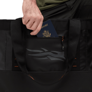 Black 40L tote bag with zip pocket and front logo, holding a passport