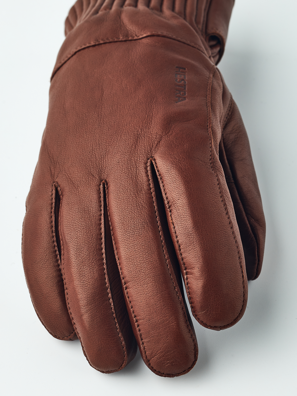 Brown leather gloves with stitched finger panels and cuff strap at wrist
