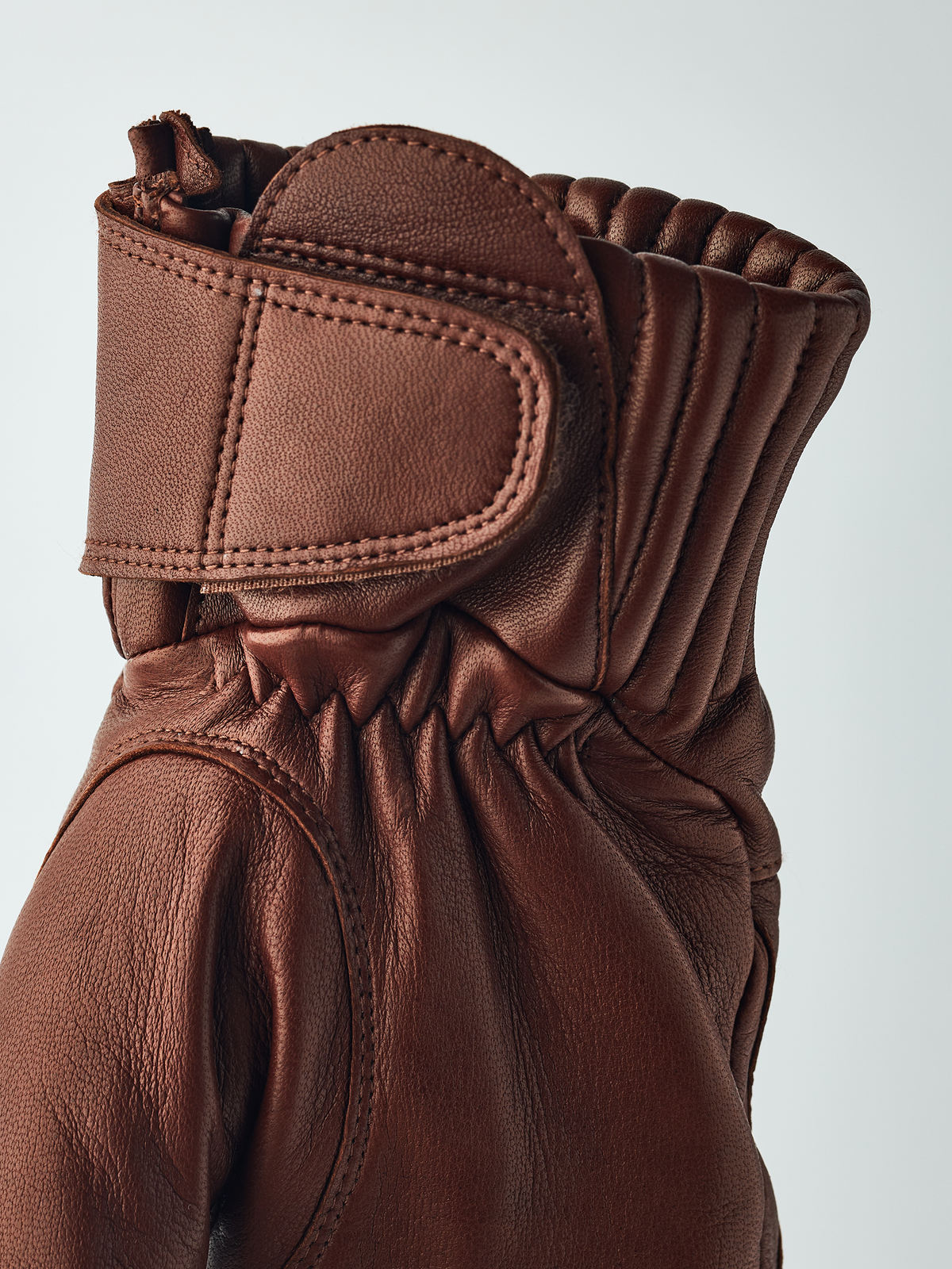 Brown leather gloves with padded wrist cuff, snap tab, and gathered fabric