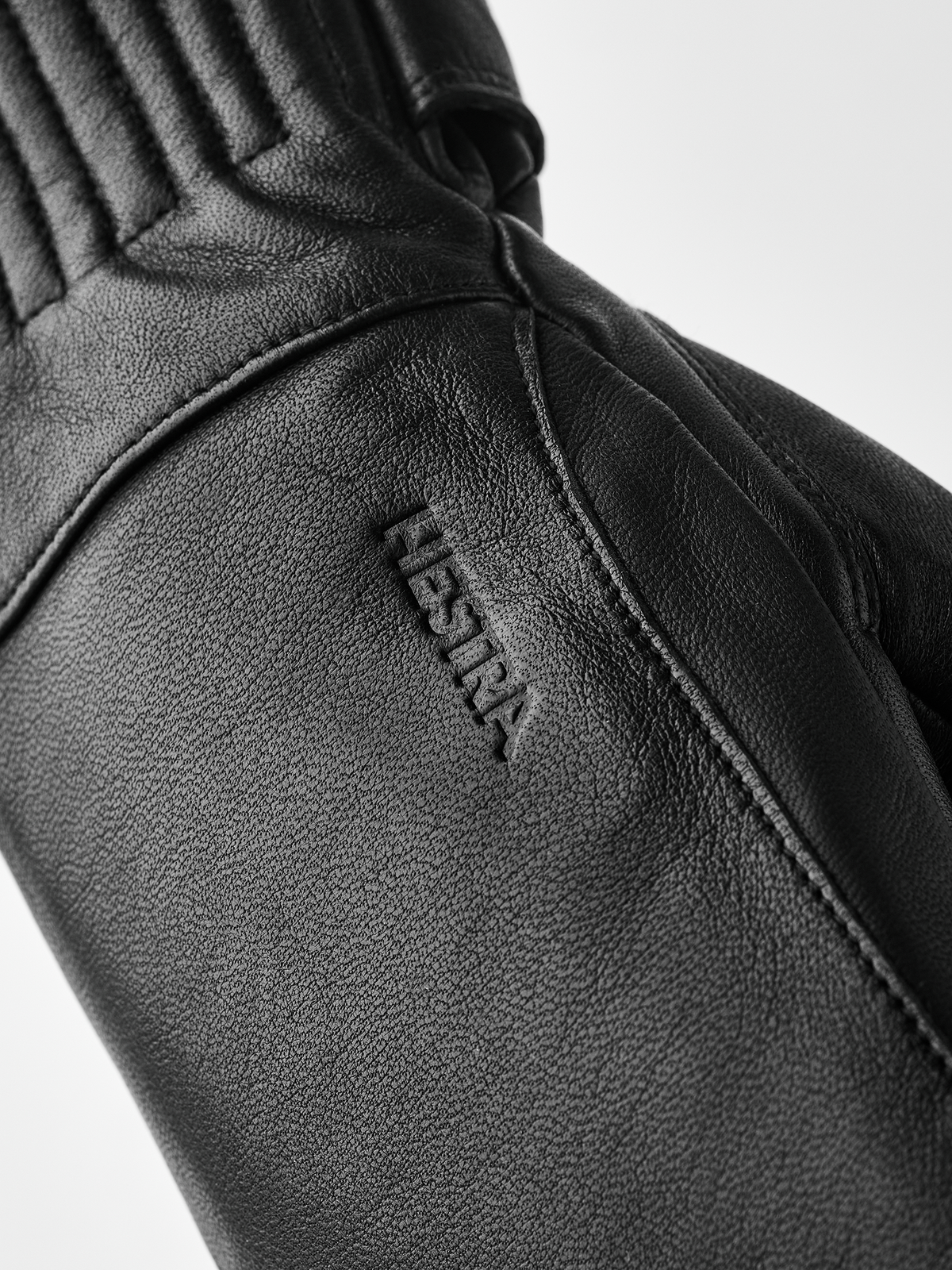 Black wool mittens detail, Hestra logo on textured leather wrist seam
