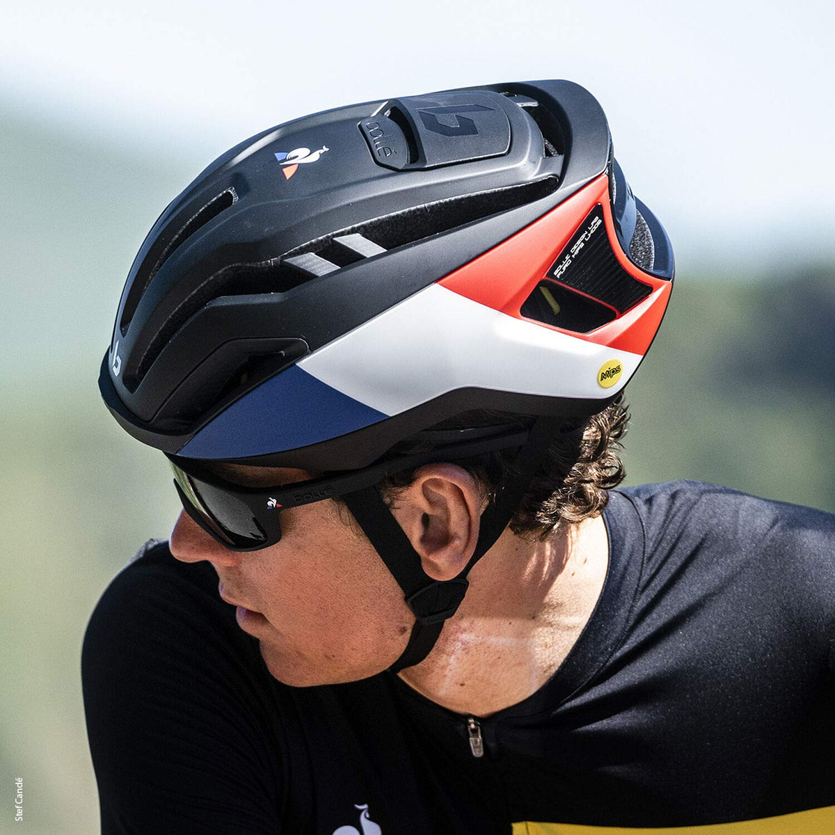 Road bike helmet in white, red, and blue worn by a cyclist, with chin strap