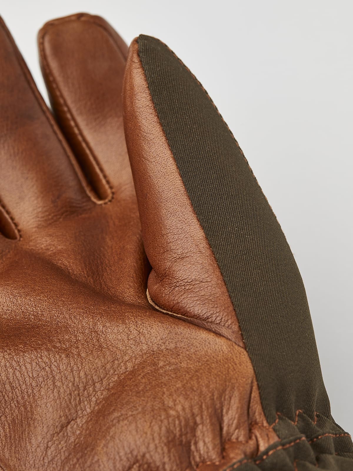 Close-up of brown leather palm and finger seams with dark olive outer panel.