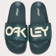 Pair of men's slide sandals, dark teal footbeds with large white Oakley letters