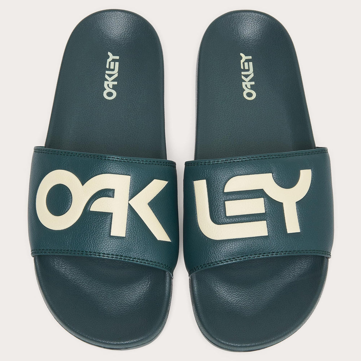 Pair of men's slide sandals, dark teal footbeds with large white Oakley letters