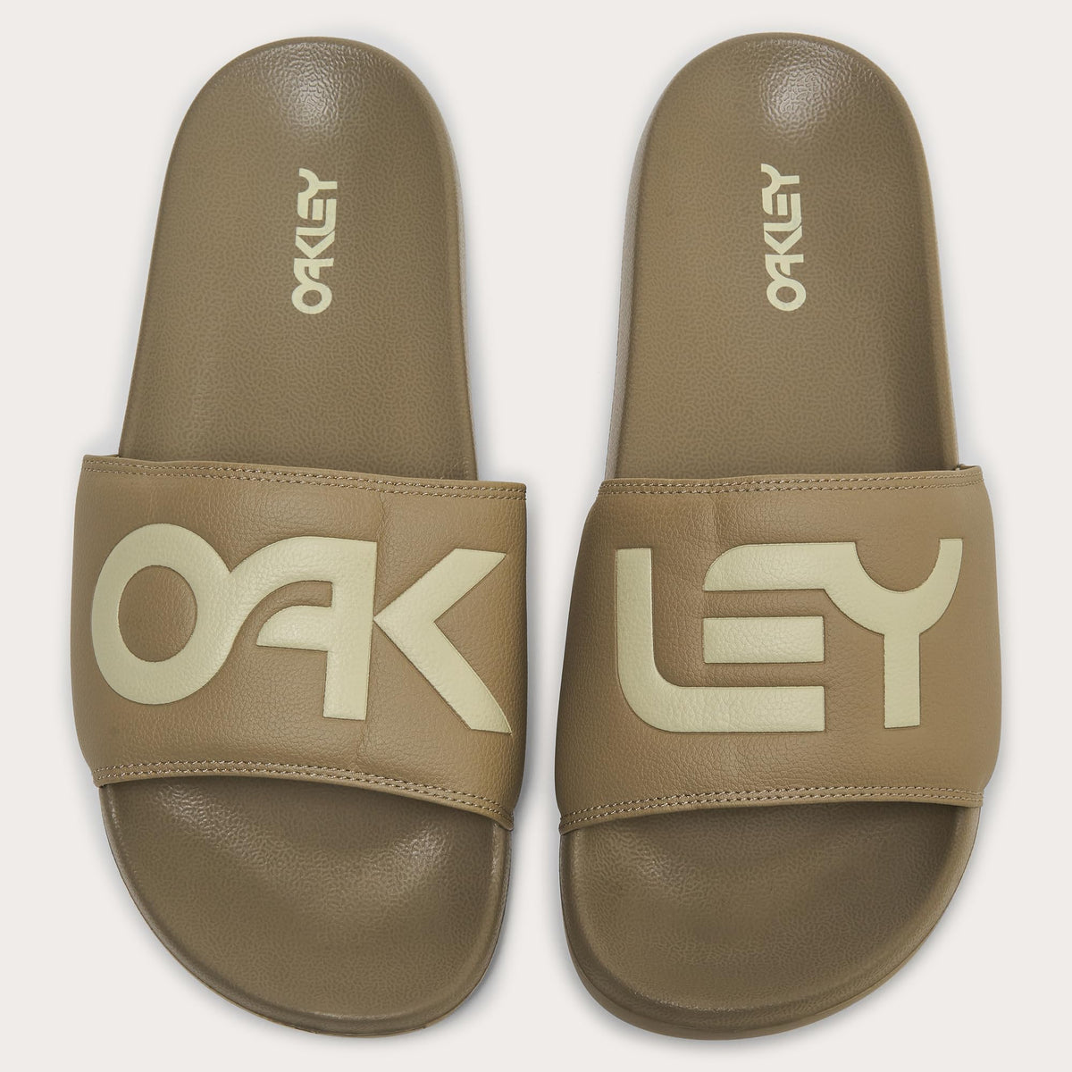 Pair of men's slide sandals, tan footbeds with Oakley logo on the straps