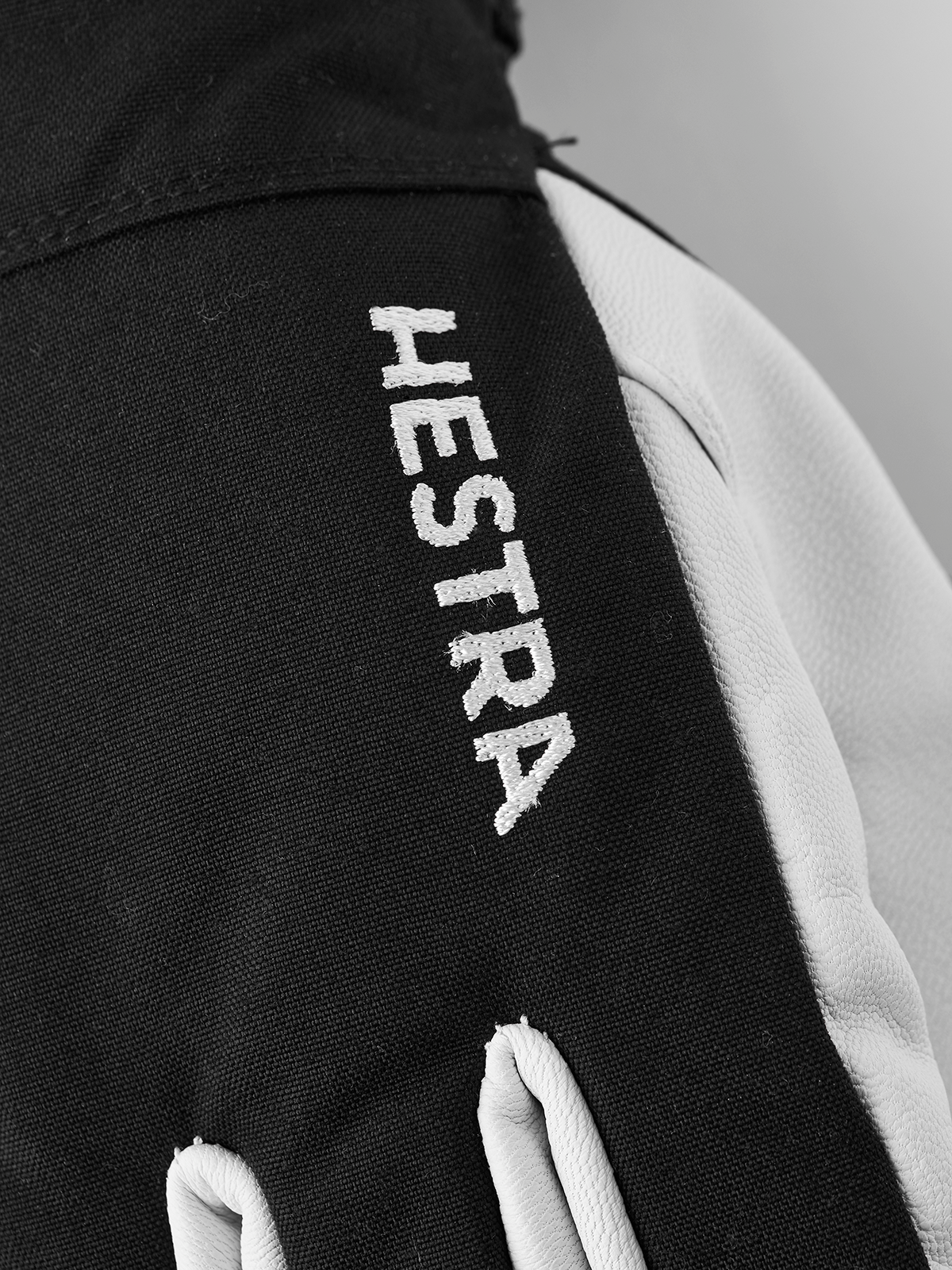 Black ski glove with vertical “HESTRA” lettering on the back.