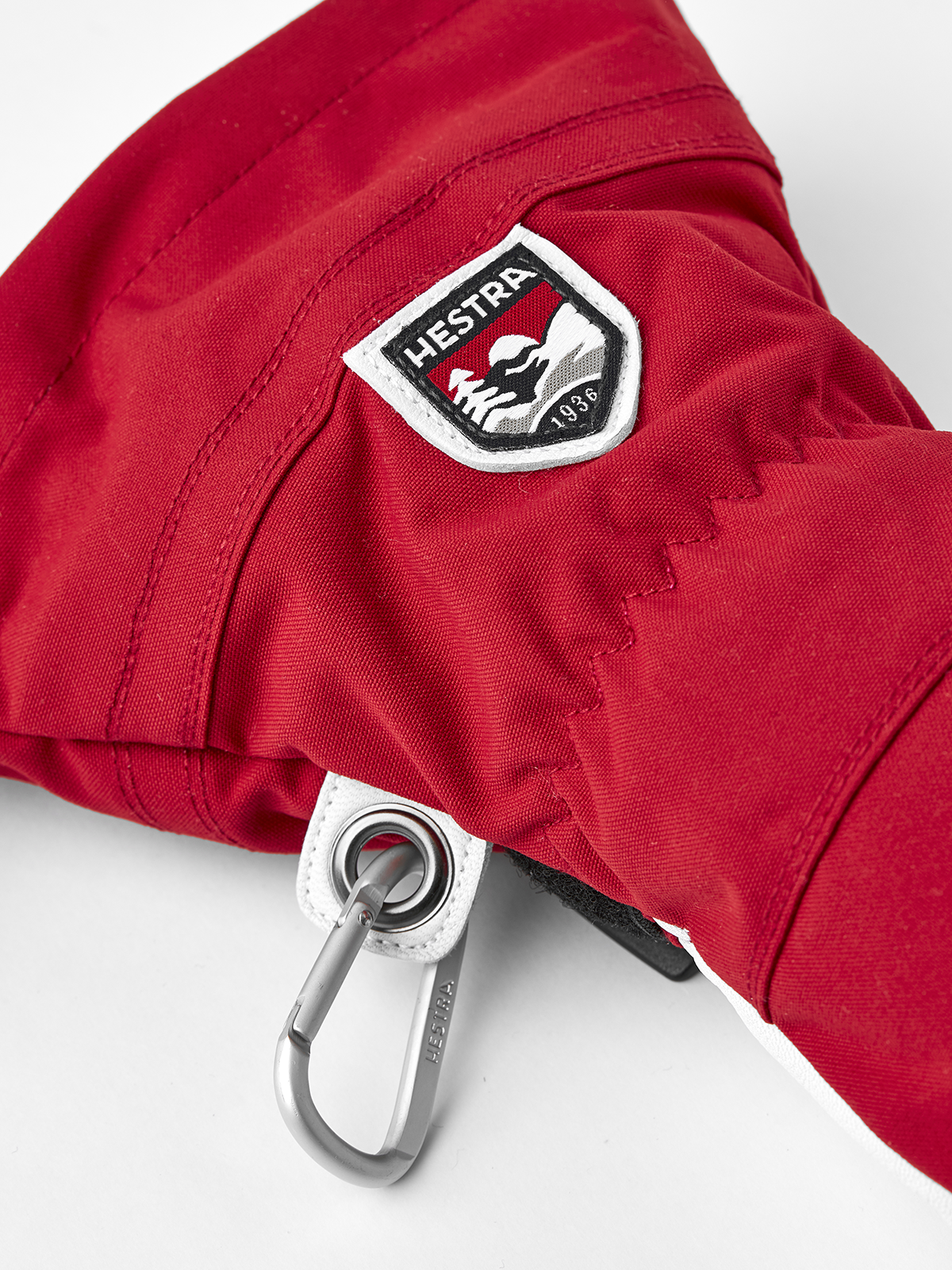 Red ski glove with Hestra logo patch and metal carabiner clip.