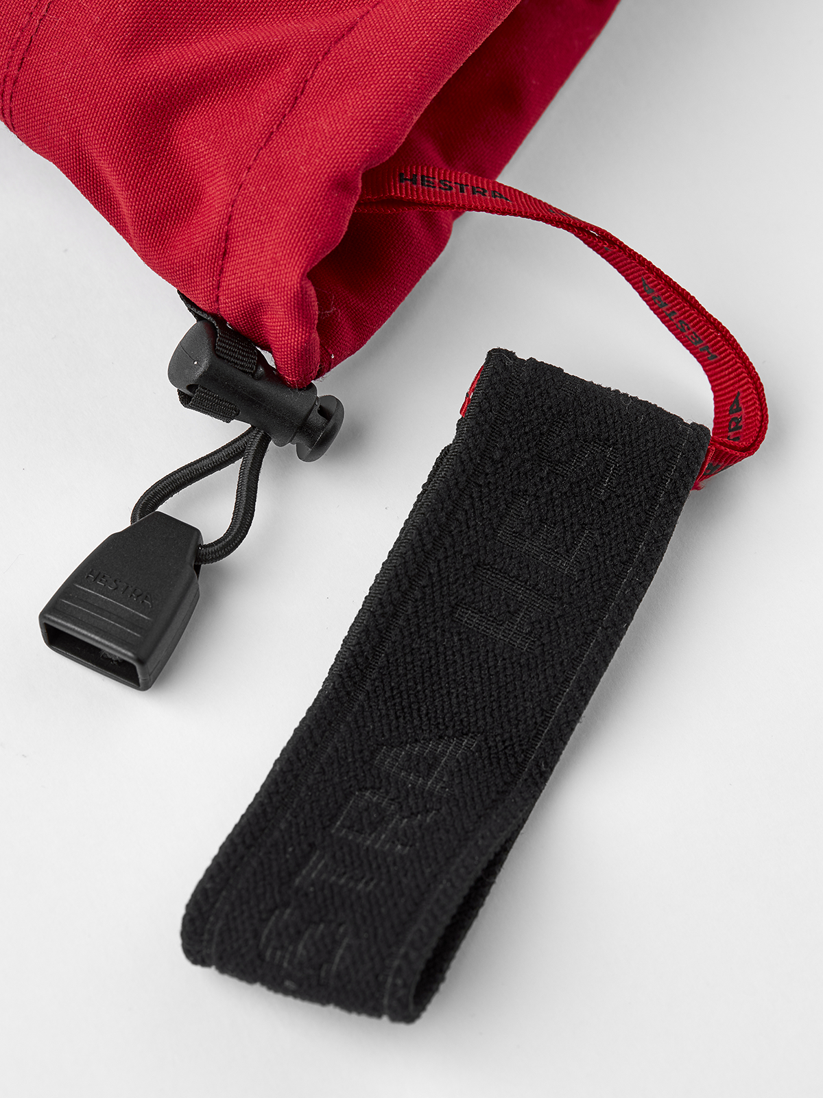 Red ski glove cuff with black pull strap and textured fabric wrist strap.