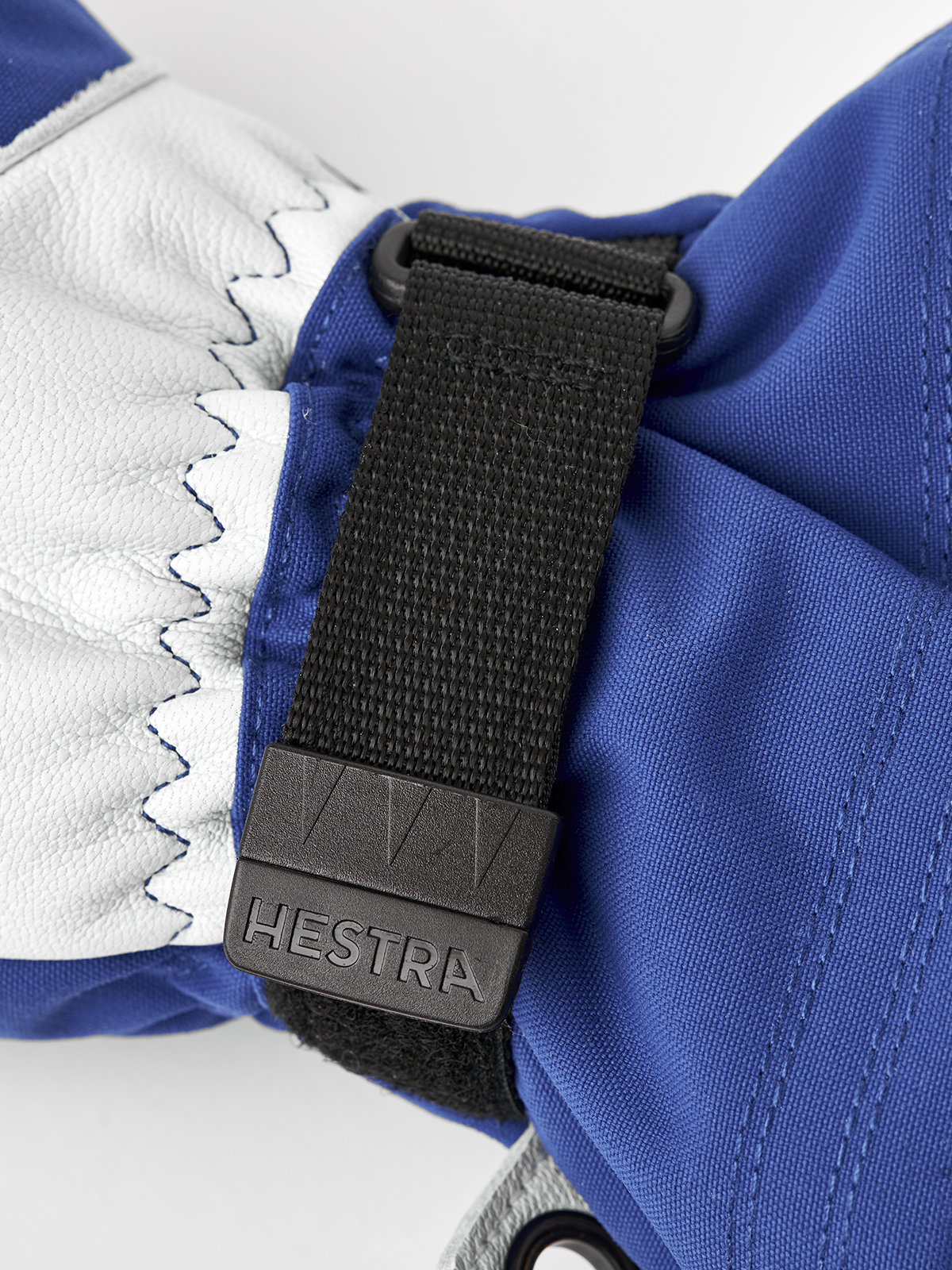 Blue and white Hestra ski mittens with black adjustable wrist strap and logo tab