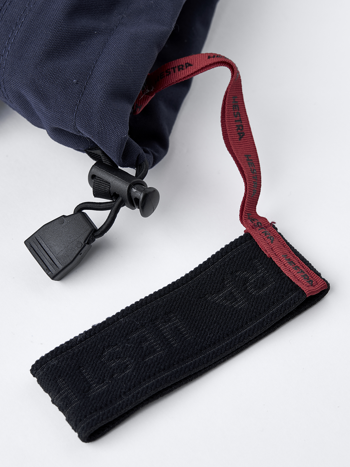 Wrist strap with red HESTRA lettering and black textured pull tab on mitten