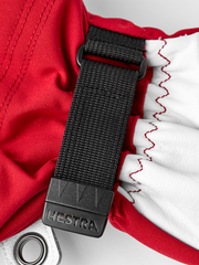 Red and white ski mitten with black strap, Hestra label, and ring clip