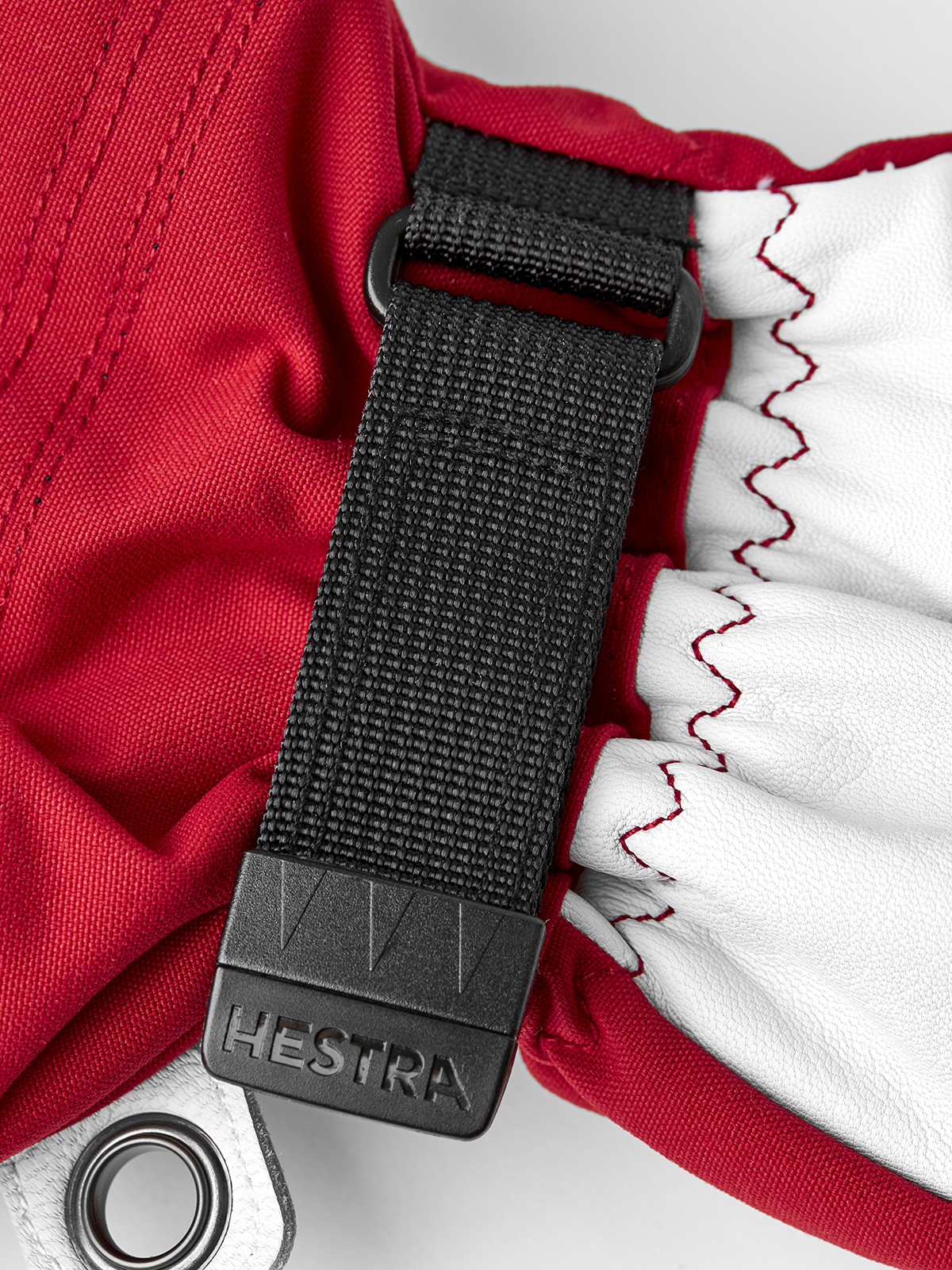 Red and white ski mitten with black strap, Hestra label, and ring clip