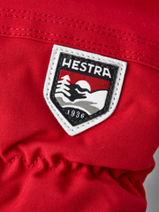 Red Hestra ski mittens with white-trim logo patch on the back