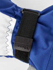 3-finger ski glove close-up with blue fabric, stitched trim, and HESTRA web strap.